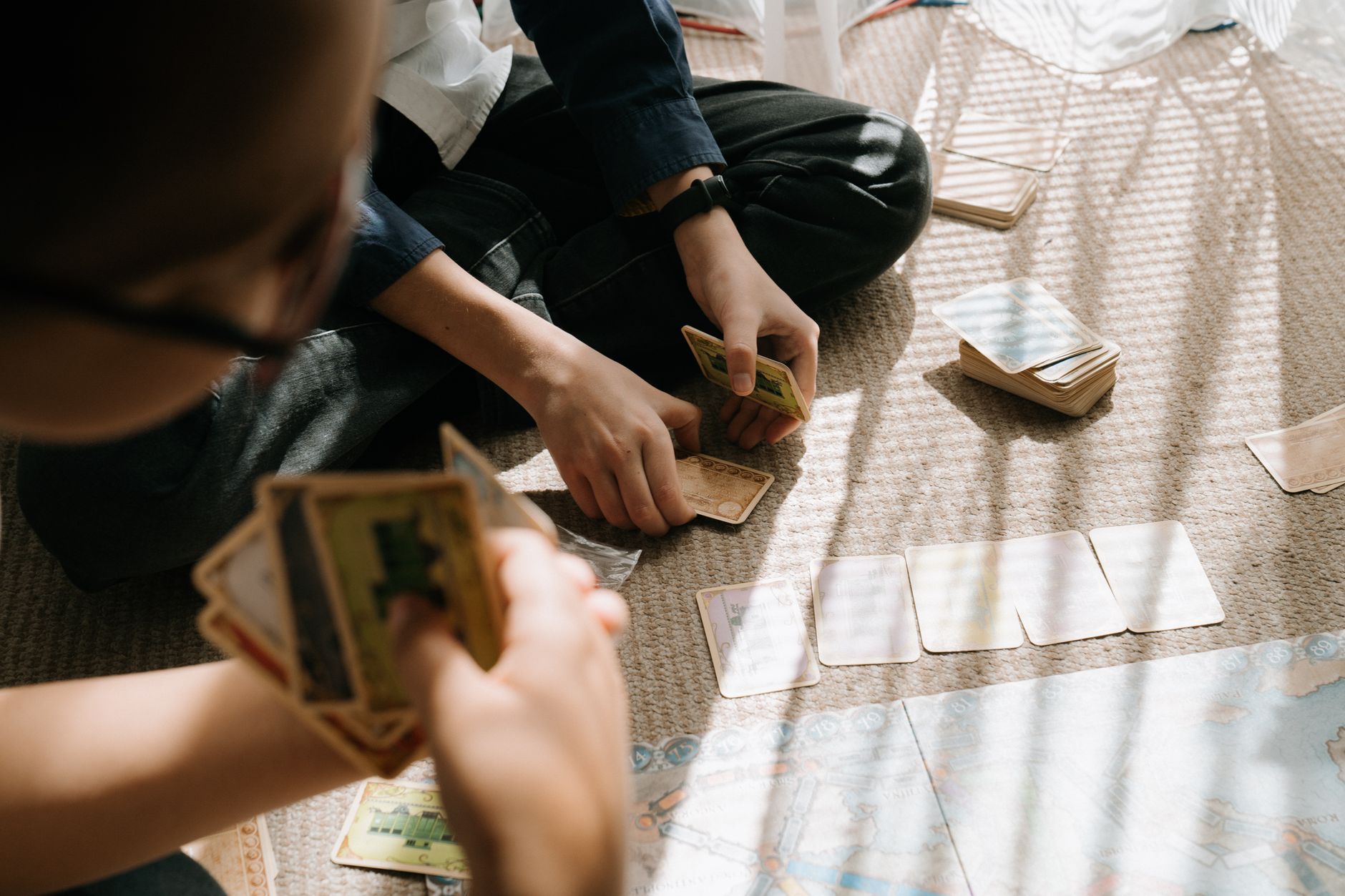 Kids engaged in an entertaining card game inside, with sunlight casting patterns on the floor.