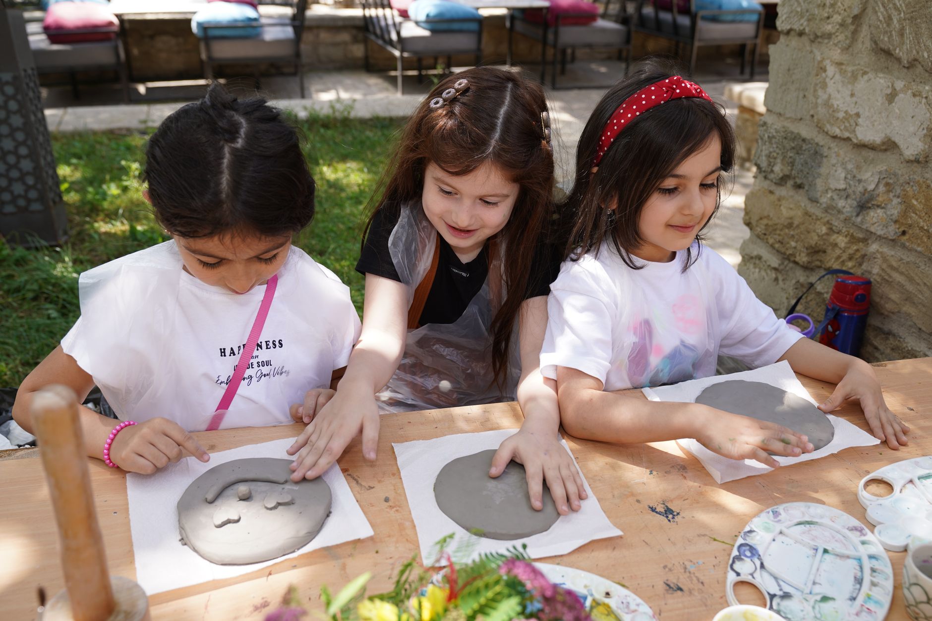 Three children crafting with clay outdoors on a sunny day. Hands-on art activity in a playful setting.