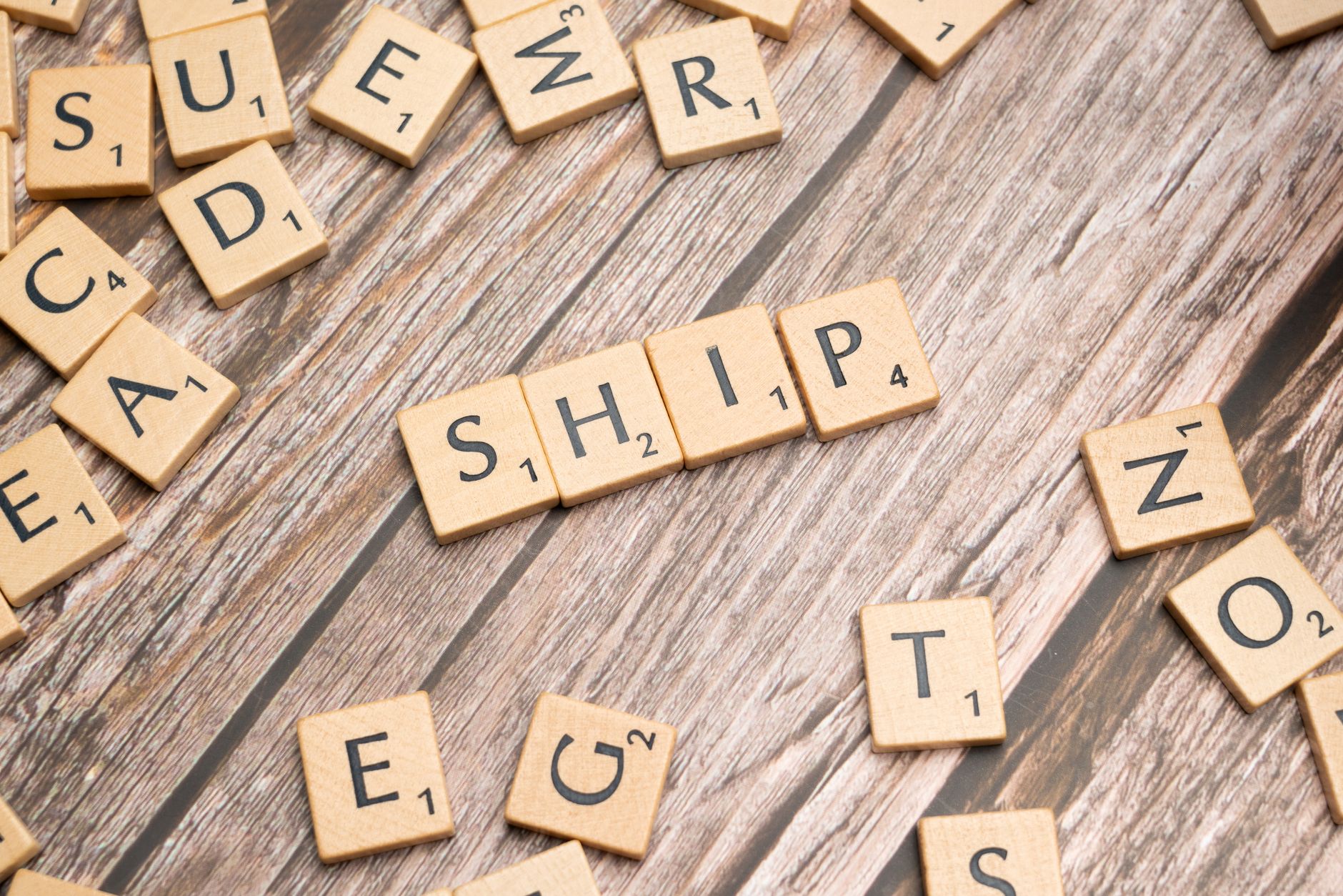 Wooden Scrabble tiles forming the word 'ship' on a rustic wooden surface.