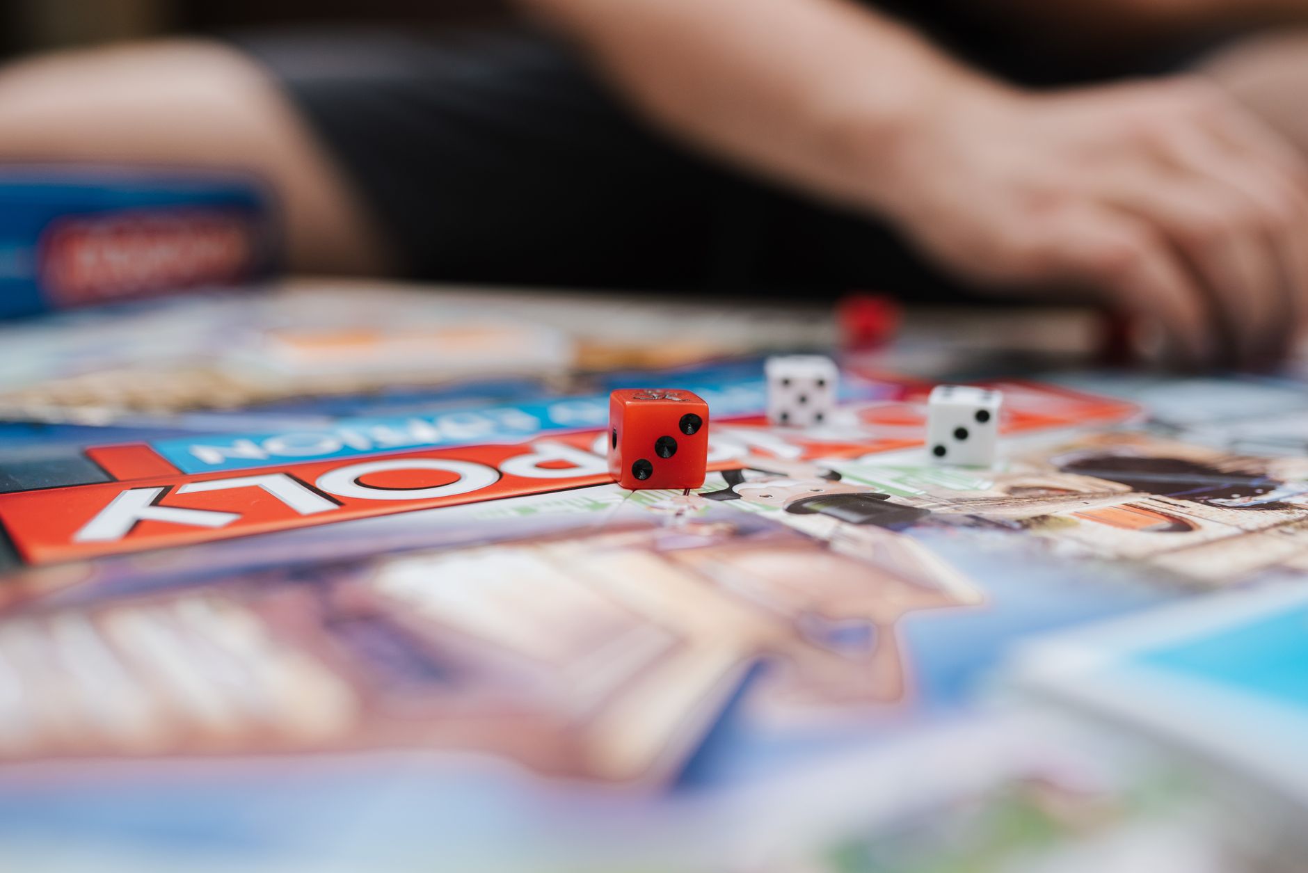 Crop anonymous person sitting at desk with game board and dices while playing Monopoly