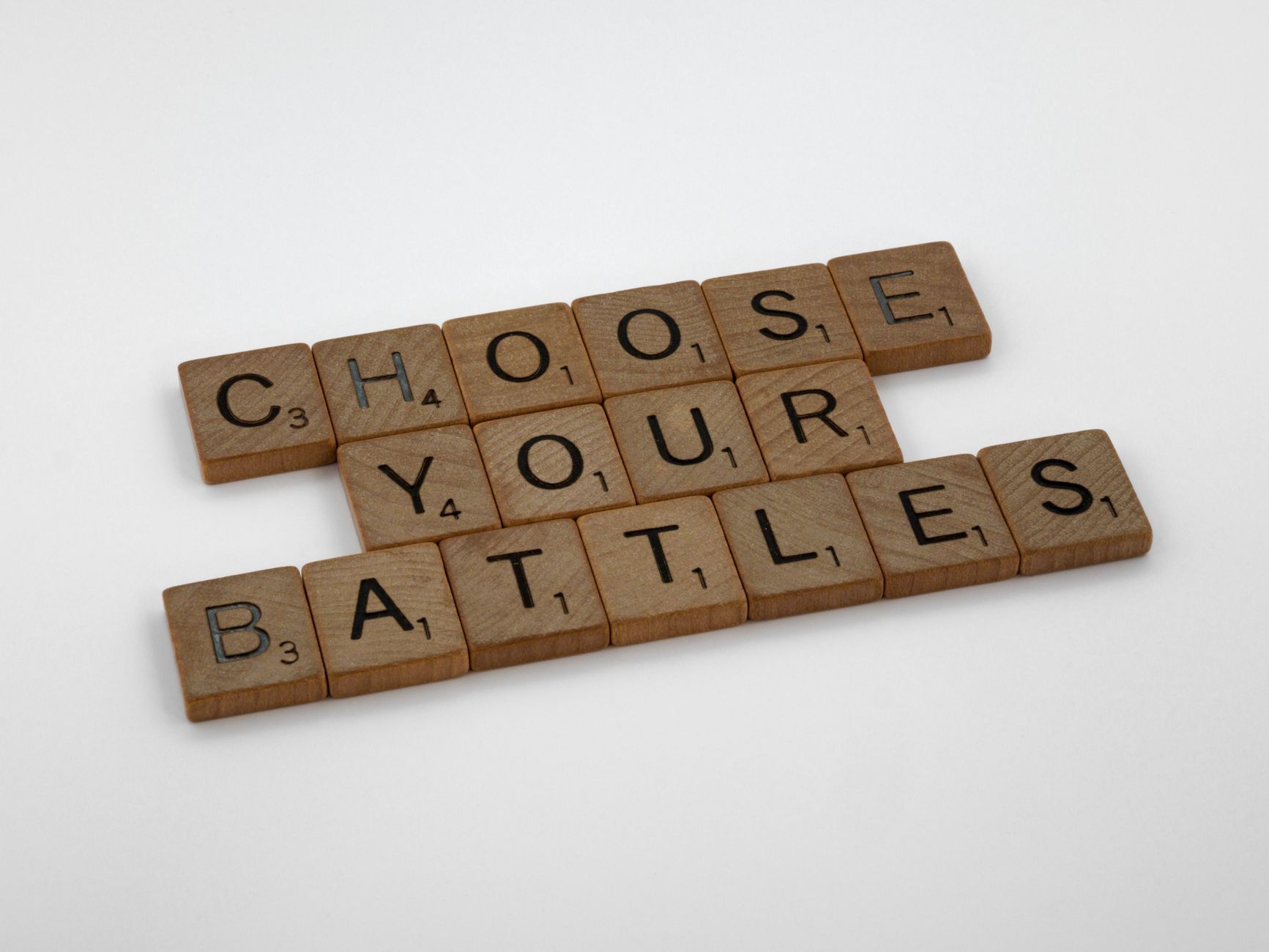 Scrabble tiles arranged to spell 'Choose Your Battles' on a white background.