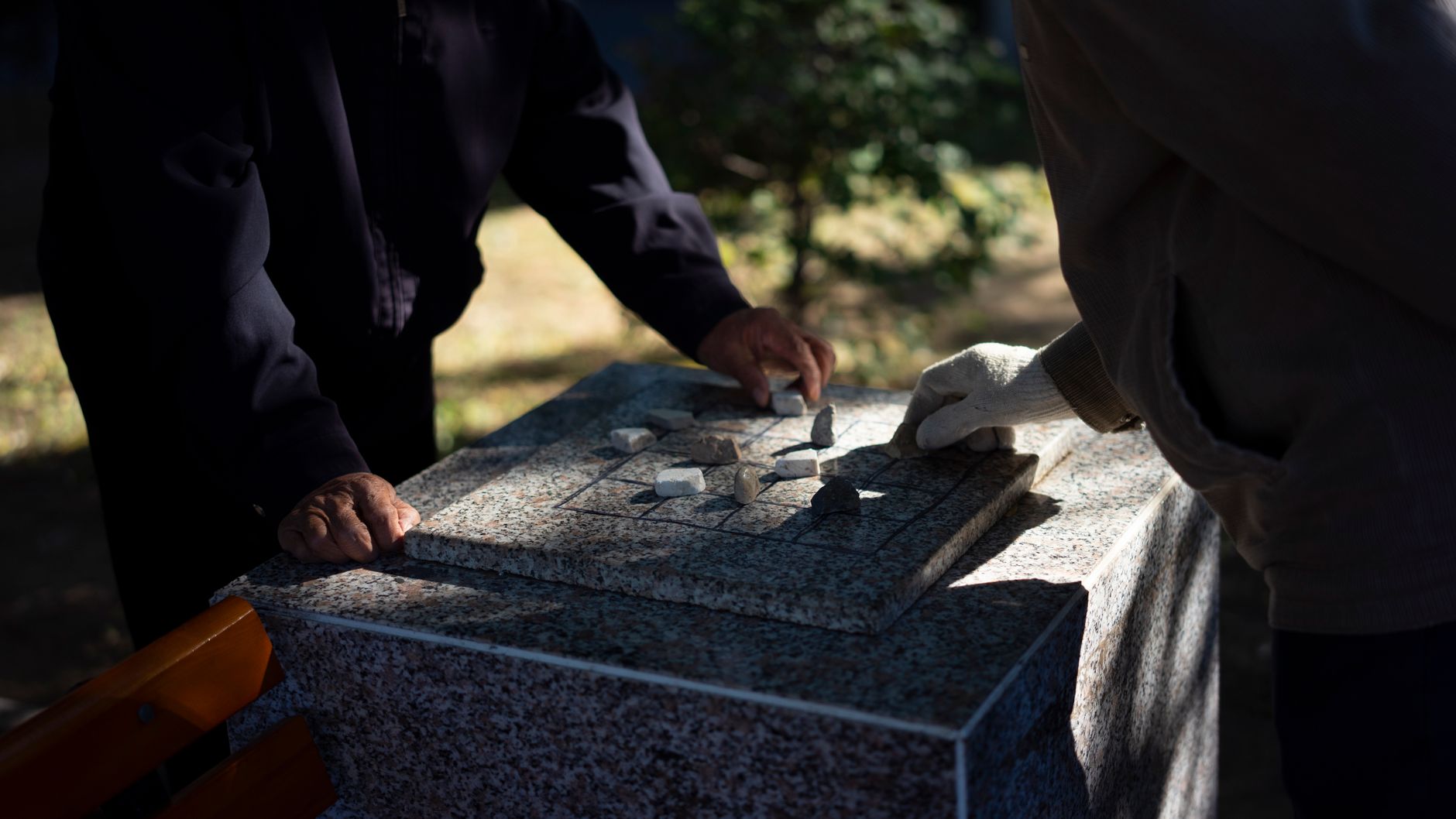 Two people play an outdoor strategy game using stones on a marble table.