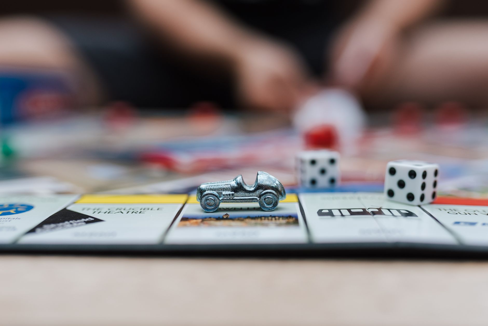 Crop anonymous man playing Monopoly at table with small plastic auto and similar dices