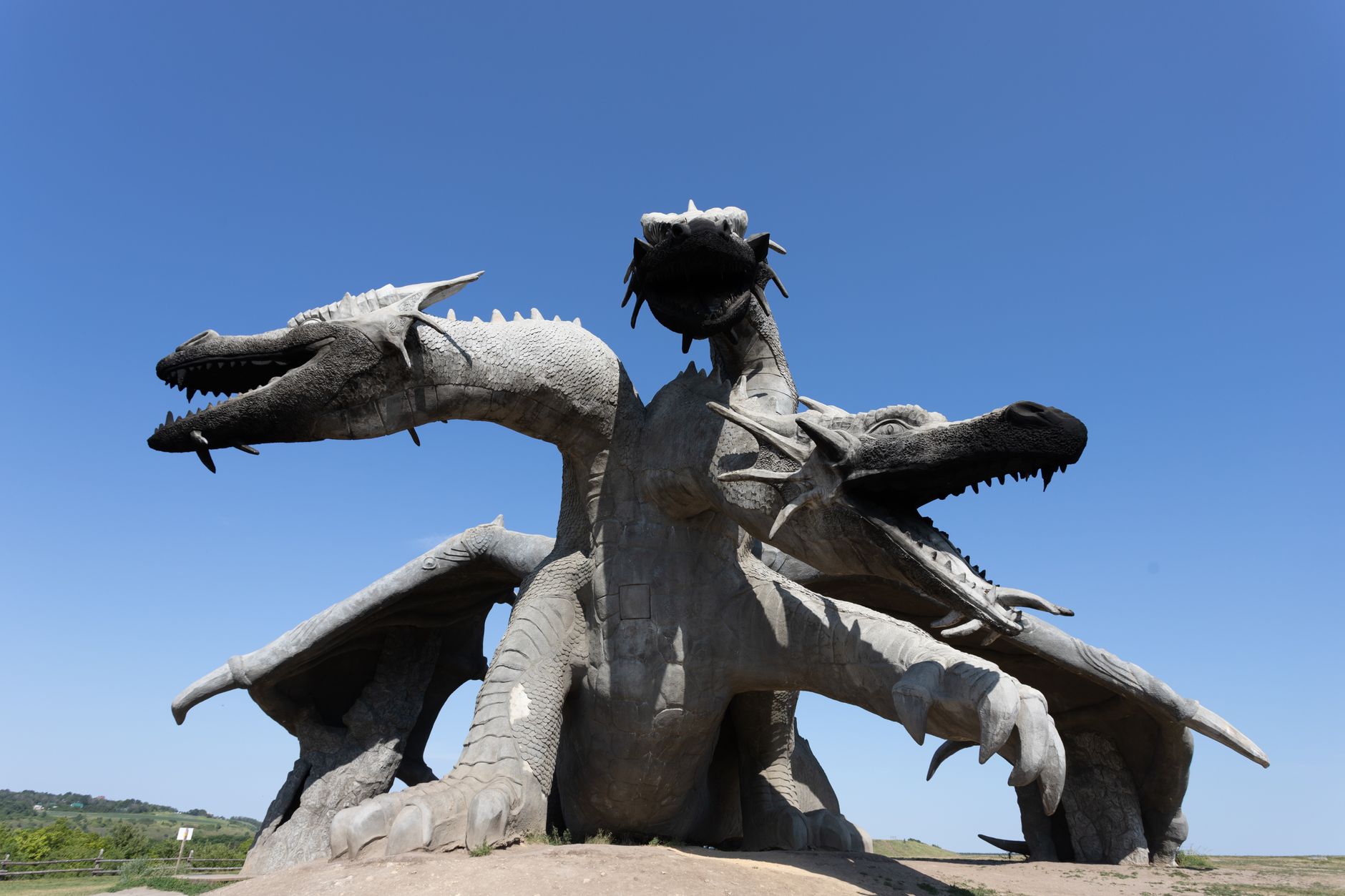 Three-headed dragon sculpture in an open landscape under a bright clear sky, showcasing intricate design and grandeur.