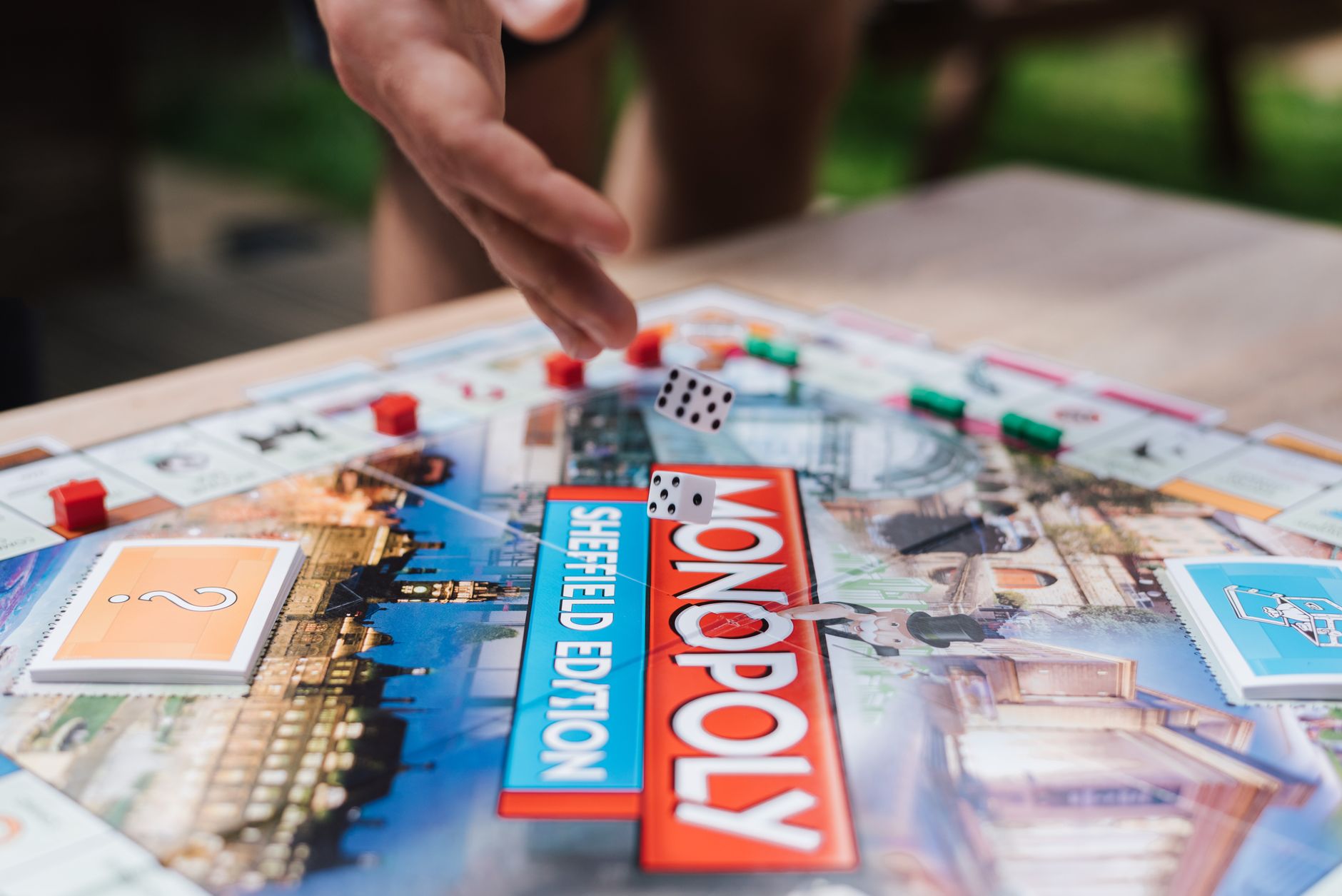 Crop unrecognizable man rolling dices while playing board game at table with cards in garden