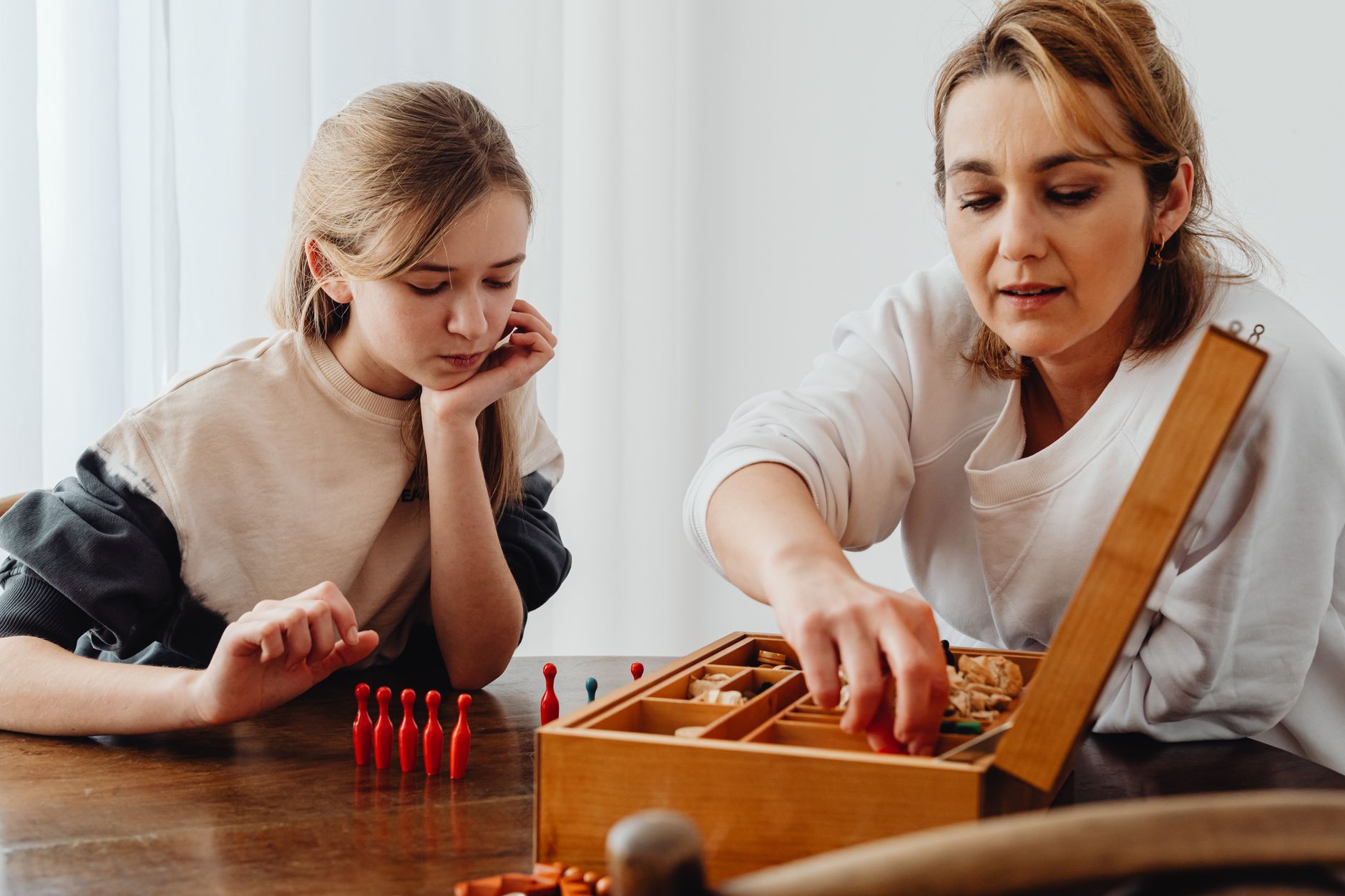 A mother and daughter enjoy a board game at the table, fostering family connection.