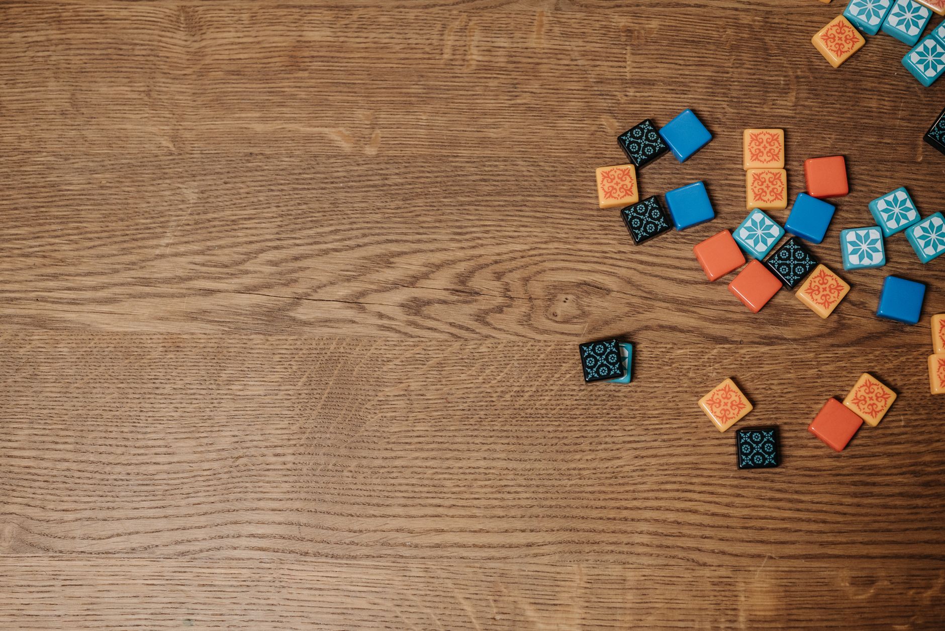 Colorful board game tiles scattered on a wooden table, offering copy space.
