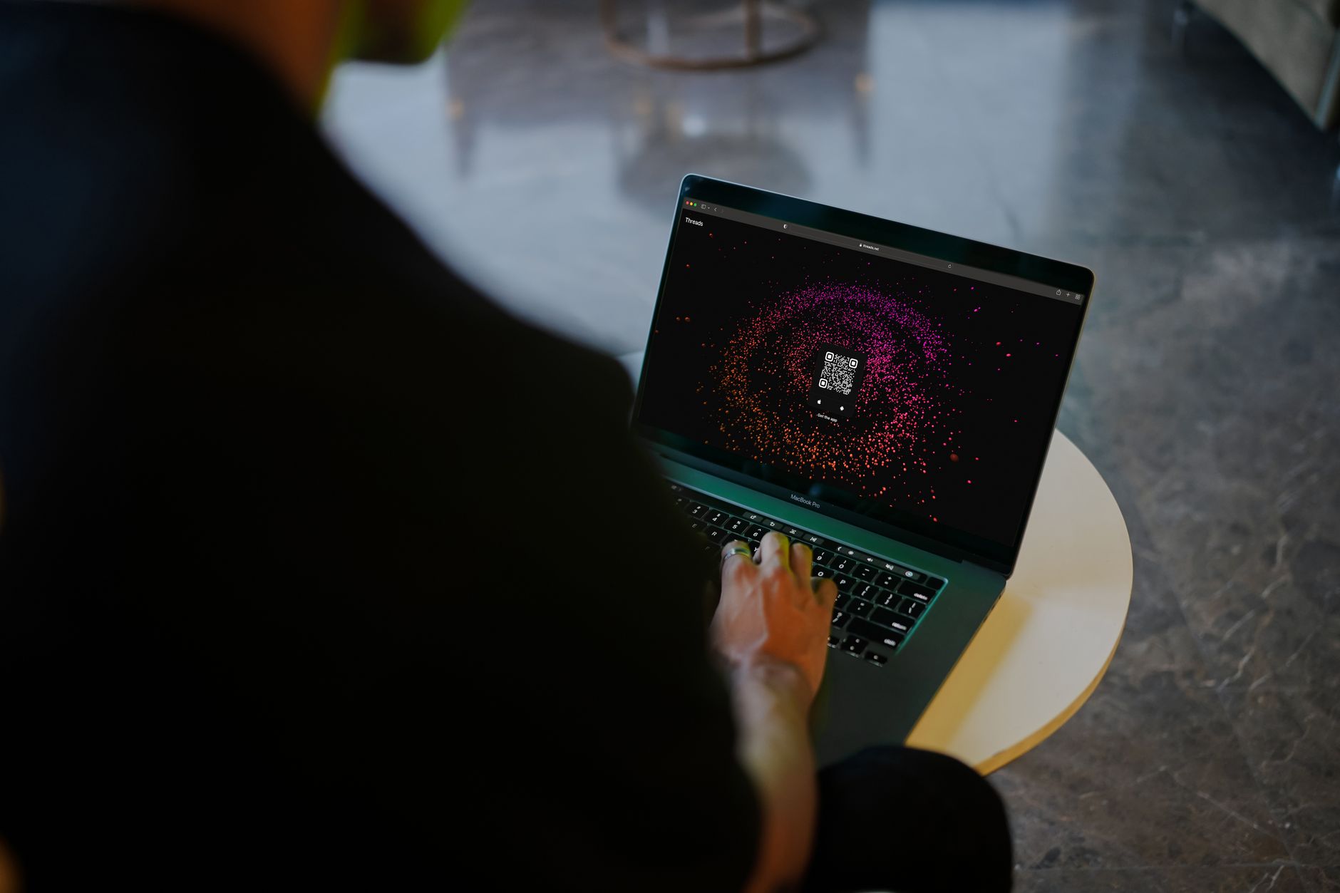 A person interacts with a colorful QR code display on a laptop in a modern indoor setting.