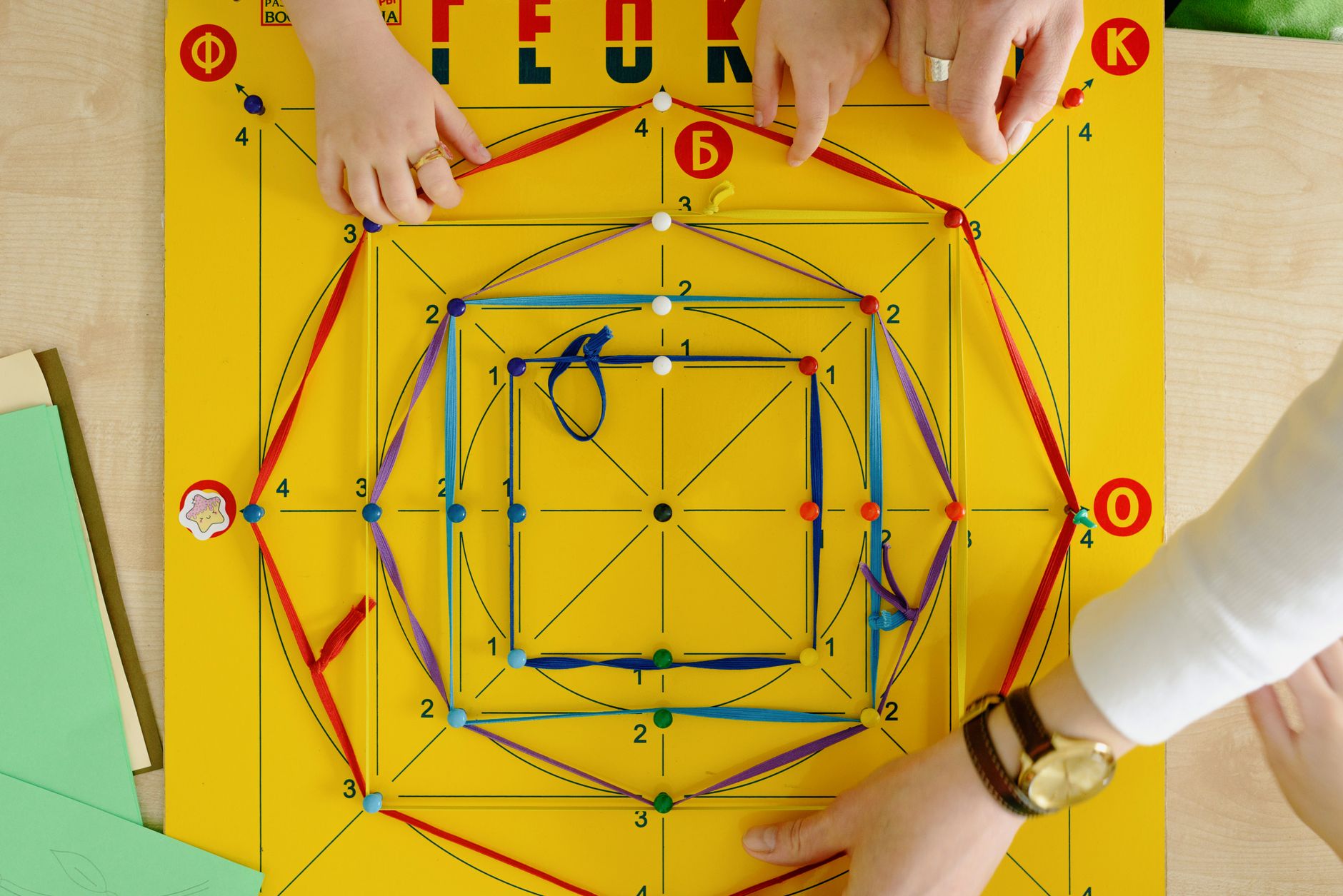 A close-up of adults and child playing an educational string game on a vibrant yellow board.