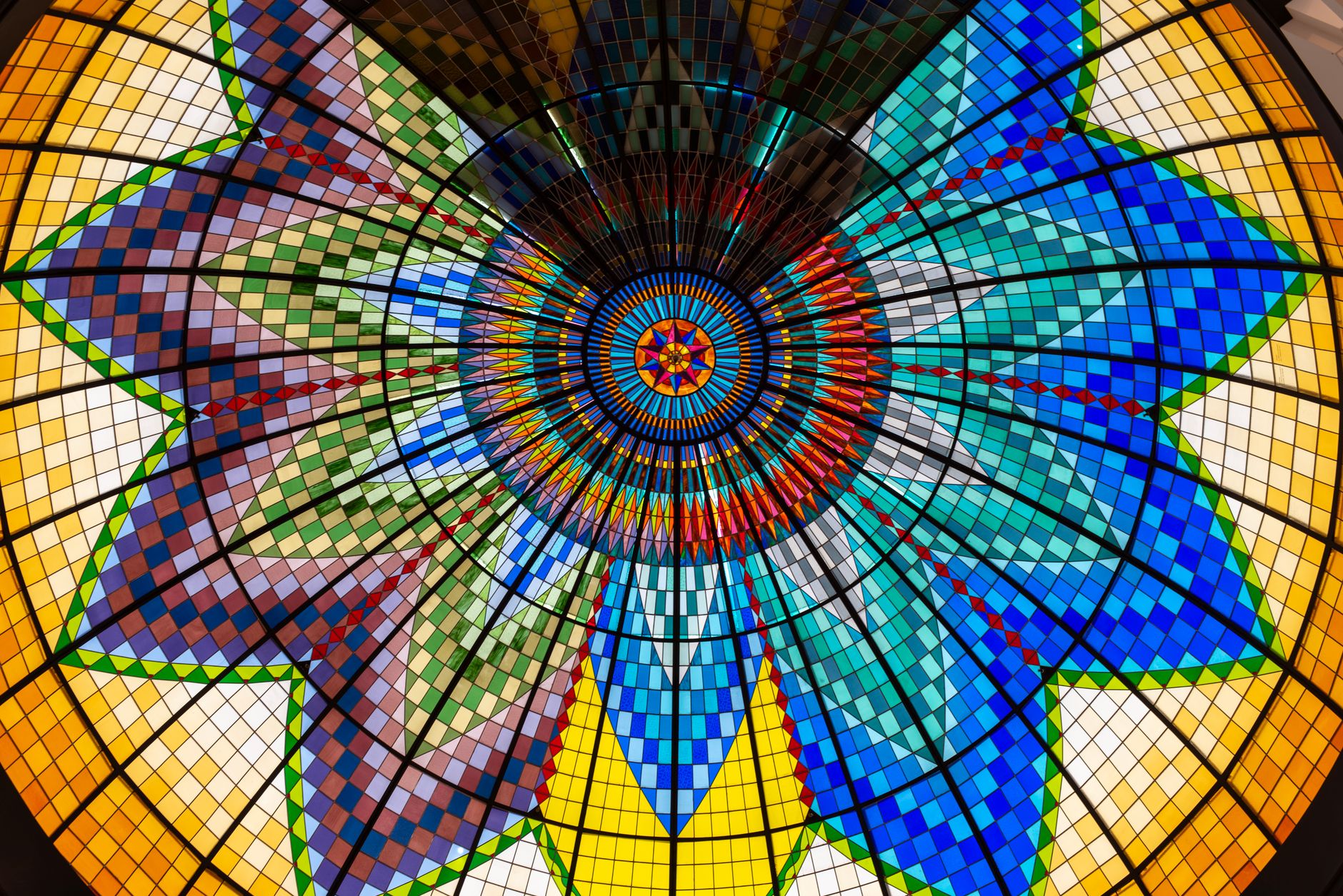 A breathtaking circular stained glass ceiling displaying vibrant geometric patterns and rich colors.