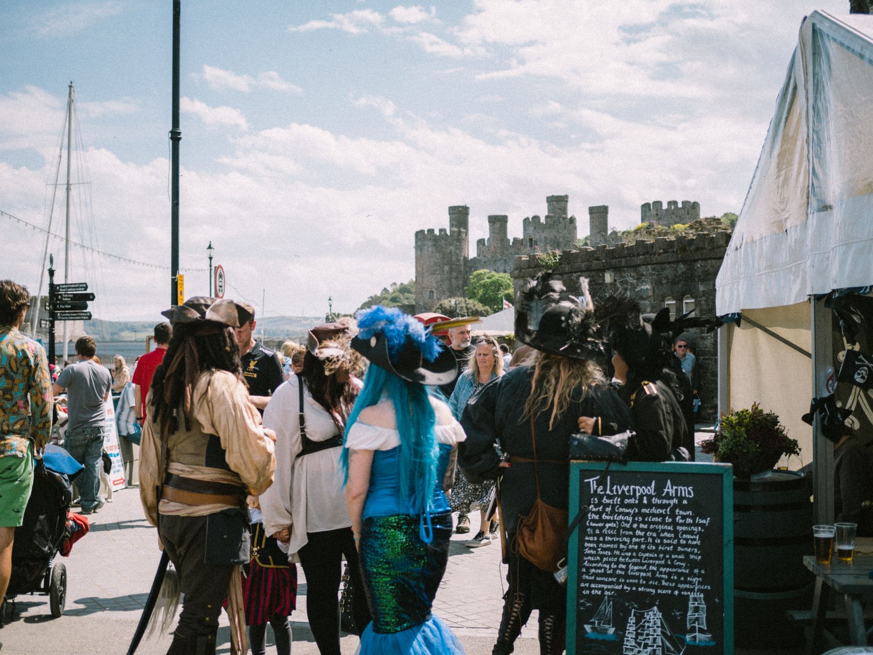 A lively medieval-themed event with attendees in costume by a historic castle.