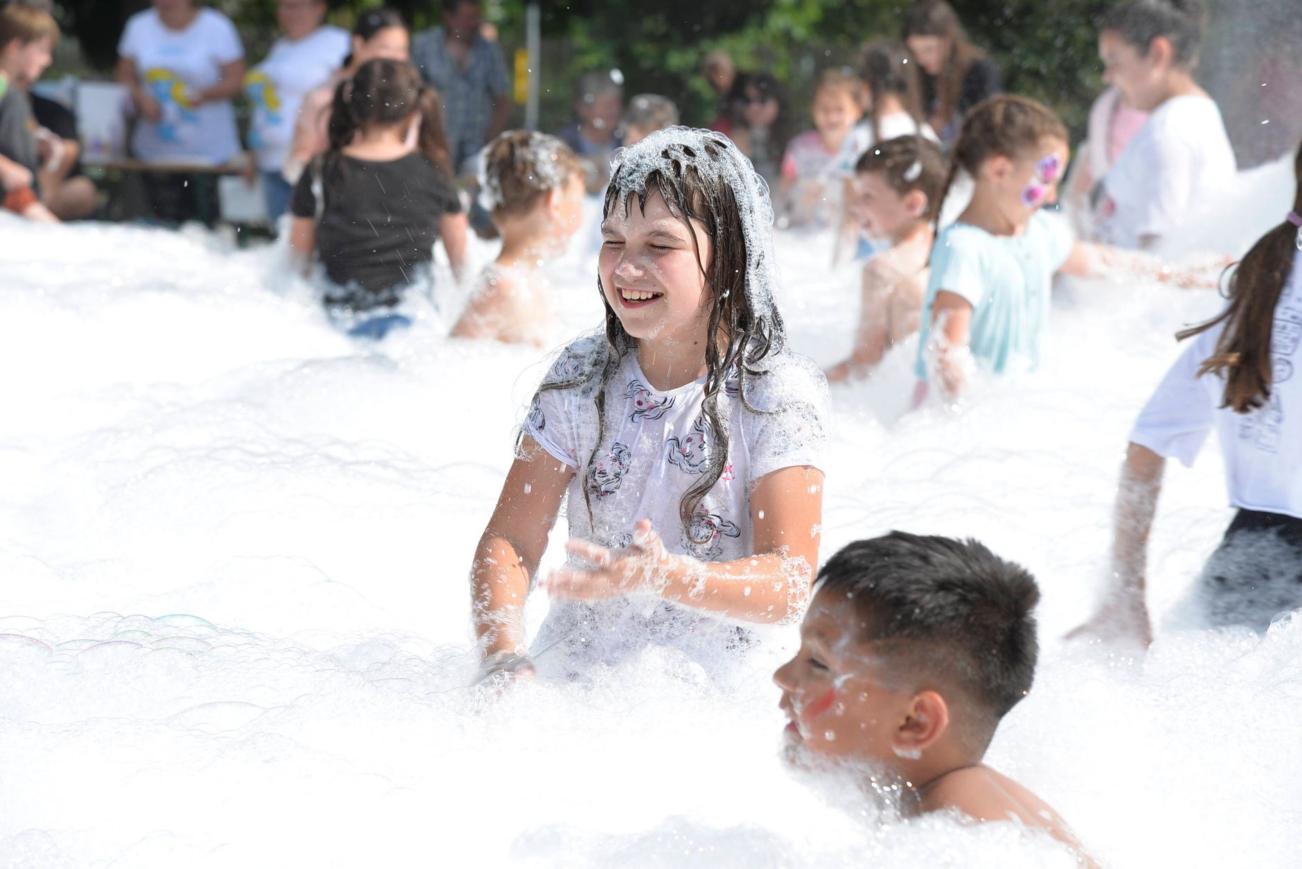 Group of children enjoying a bubbly outdoor event under sunny skies.
