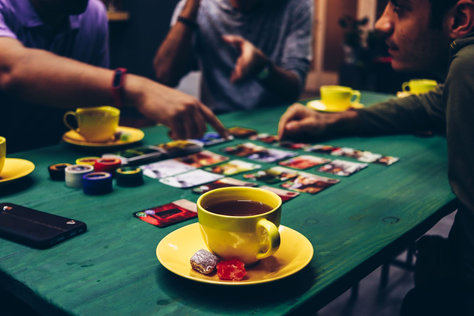 Adults enjoying a board game with tea and snacks in a cozy indoor setting.