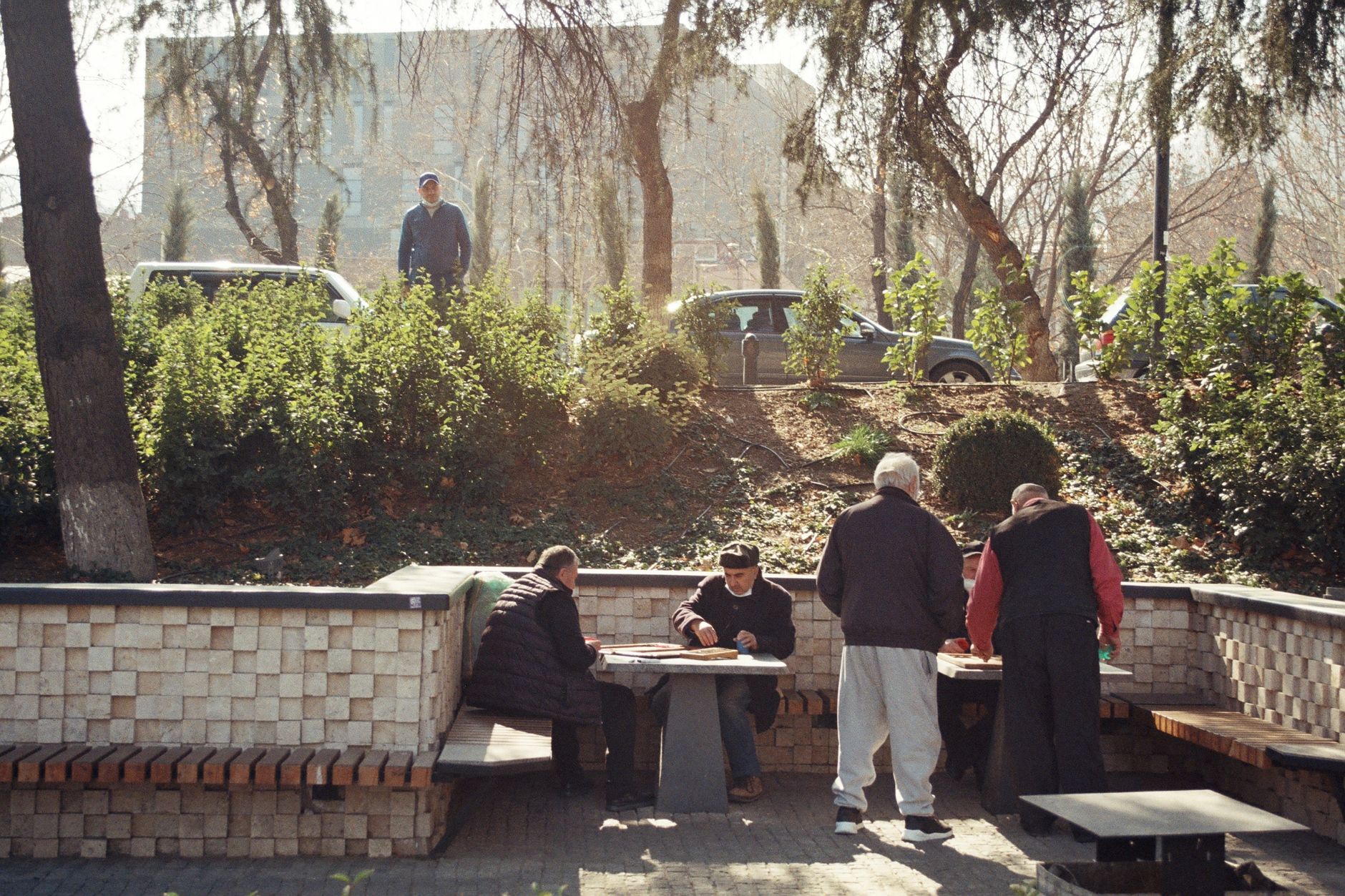 Men playing board games at outdoor park tables on a sunny day.