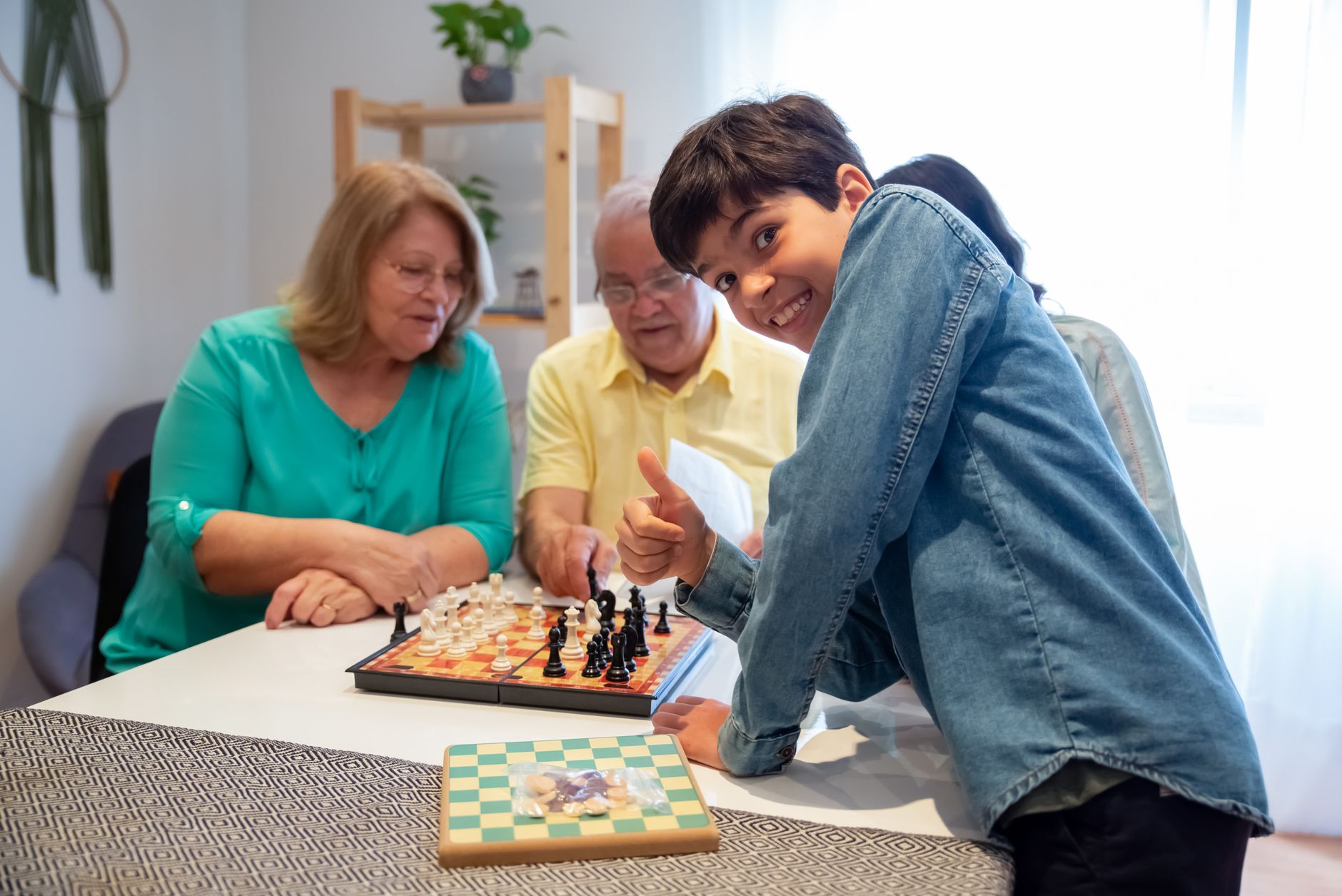 Grandparents and grandson share a joyful moment playing chess indoors.