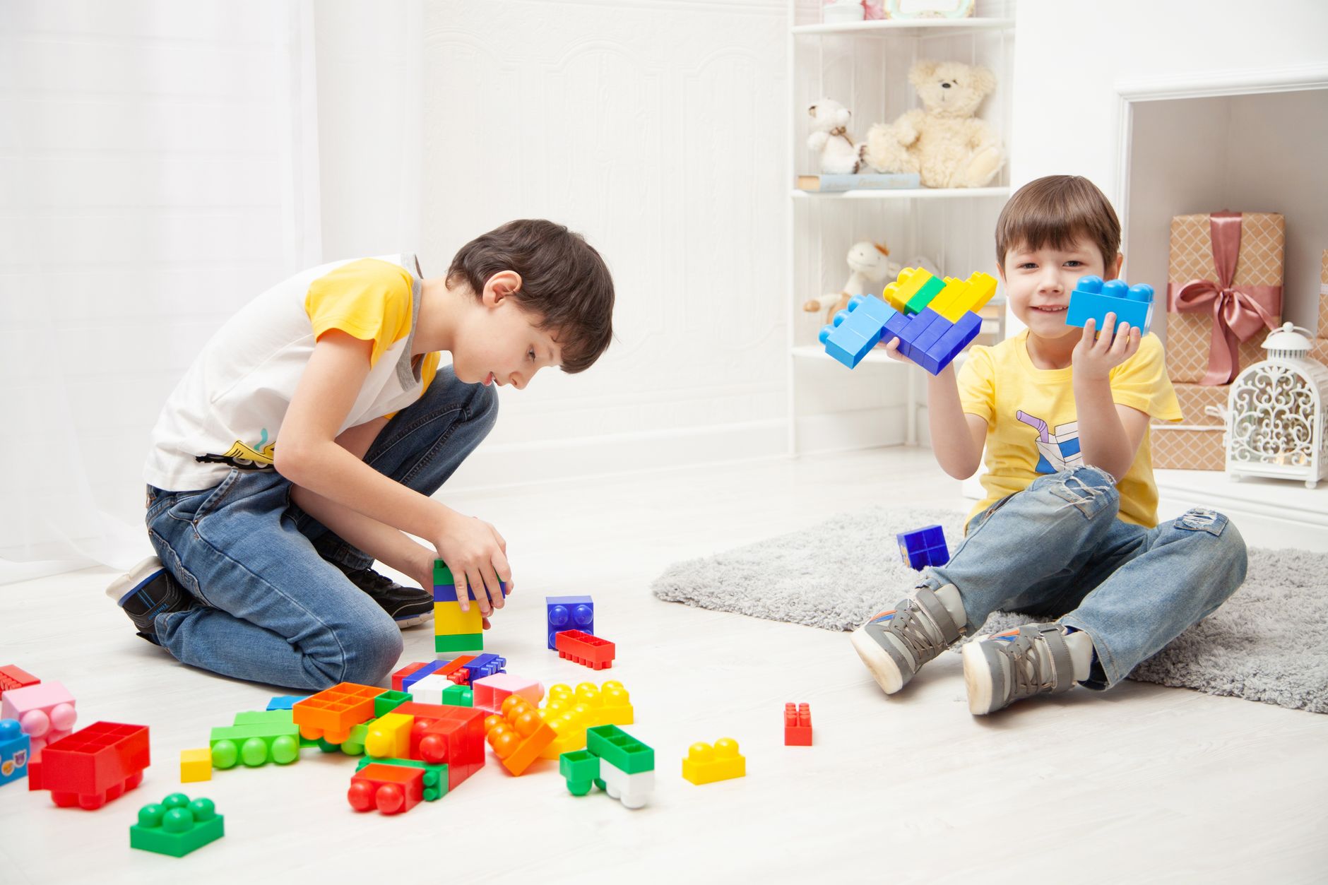 Two boys joyfully playing with colorful building blocks in a bright indoor room.
