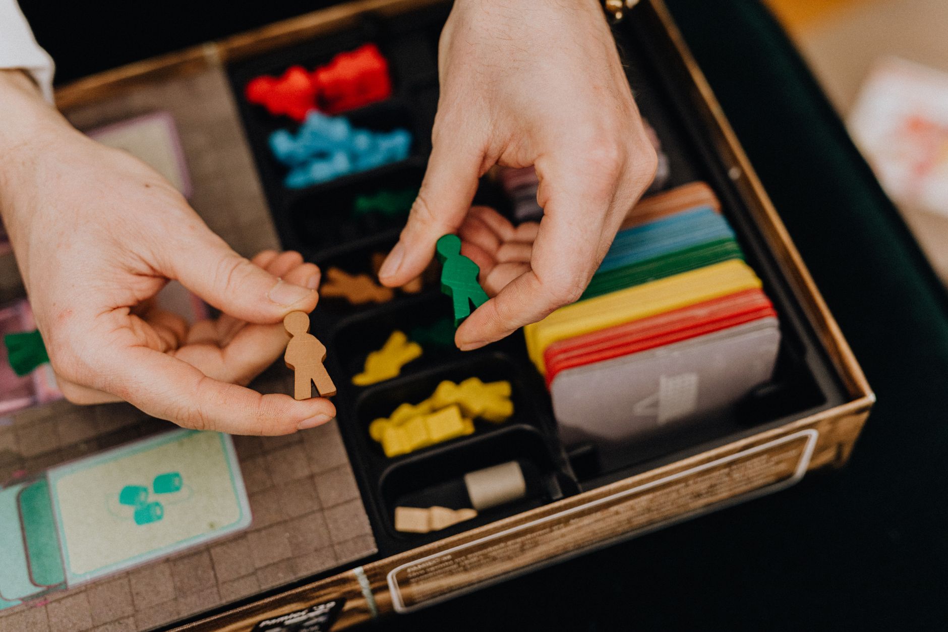 Hands arranging colorful game pieces for a board game. Promotes leisure and family fun.