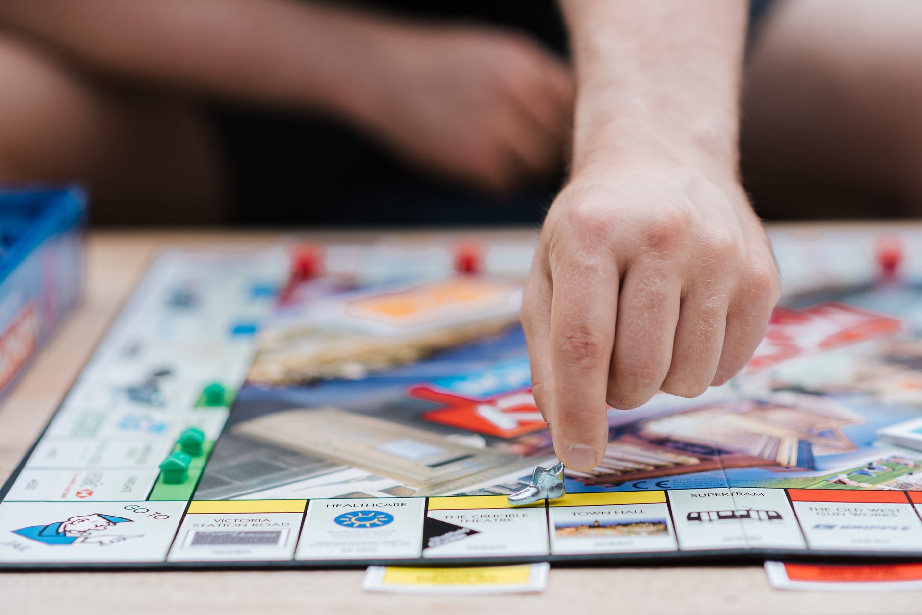 Crop anonymous male player with small artificial footwear playing Monopoly at desk in daylight