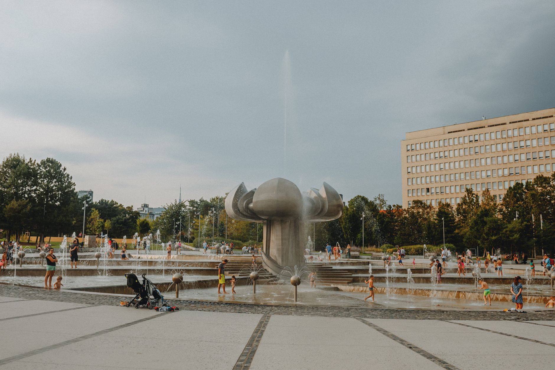 A lively urban park with a modern fountain where families and children enjoy playing in the water.