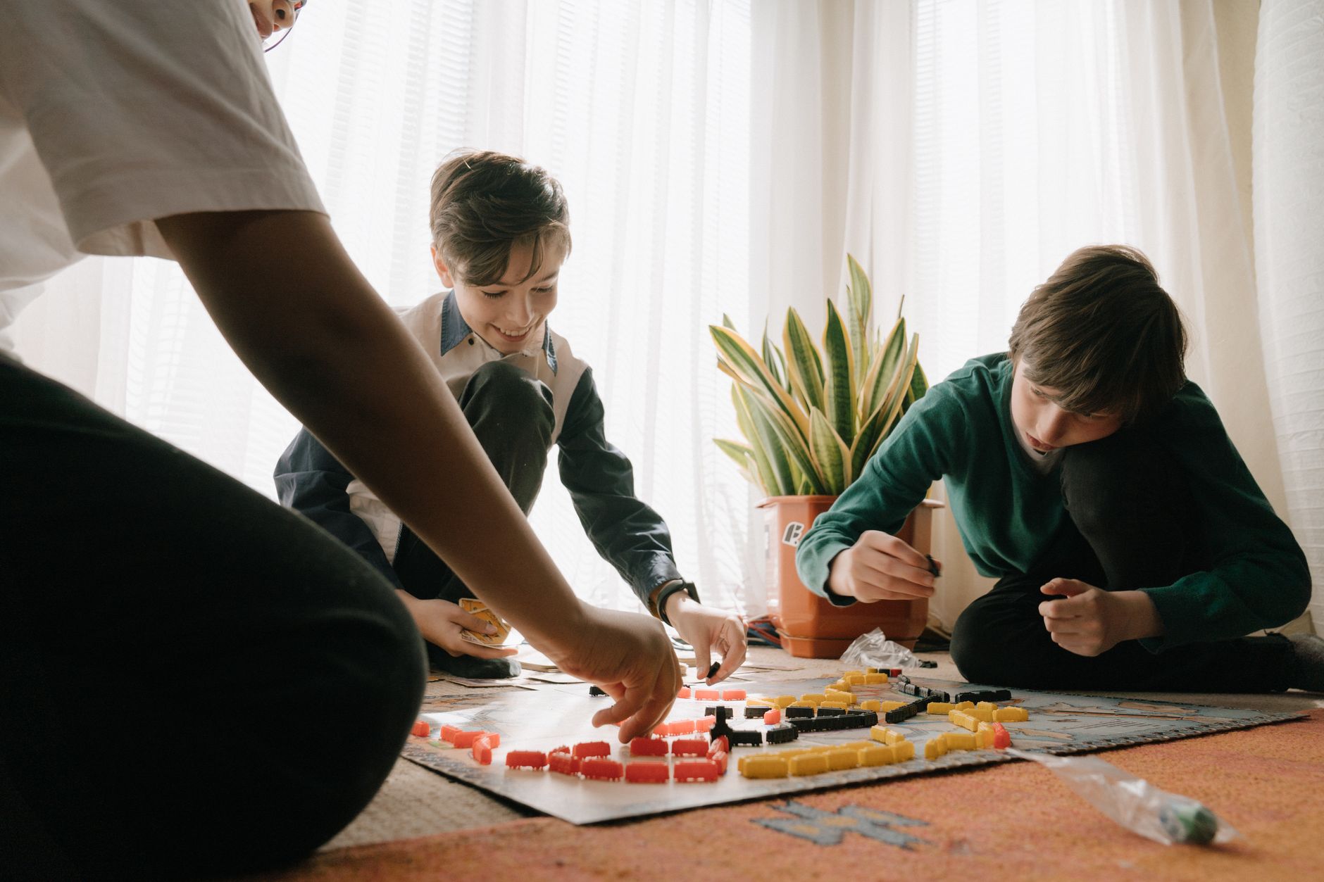 Three kids engaged in playing a strategic board game indoors, fostering fun and teamwork.