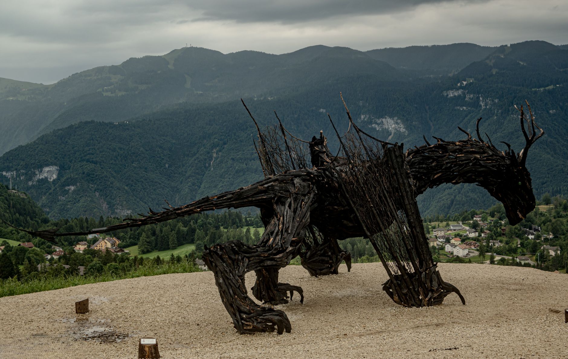 Giant wooden dragon sculpture surrounded by scenic mountains and lush greenery.