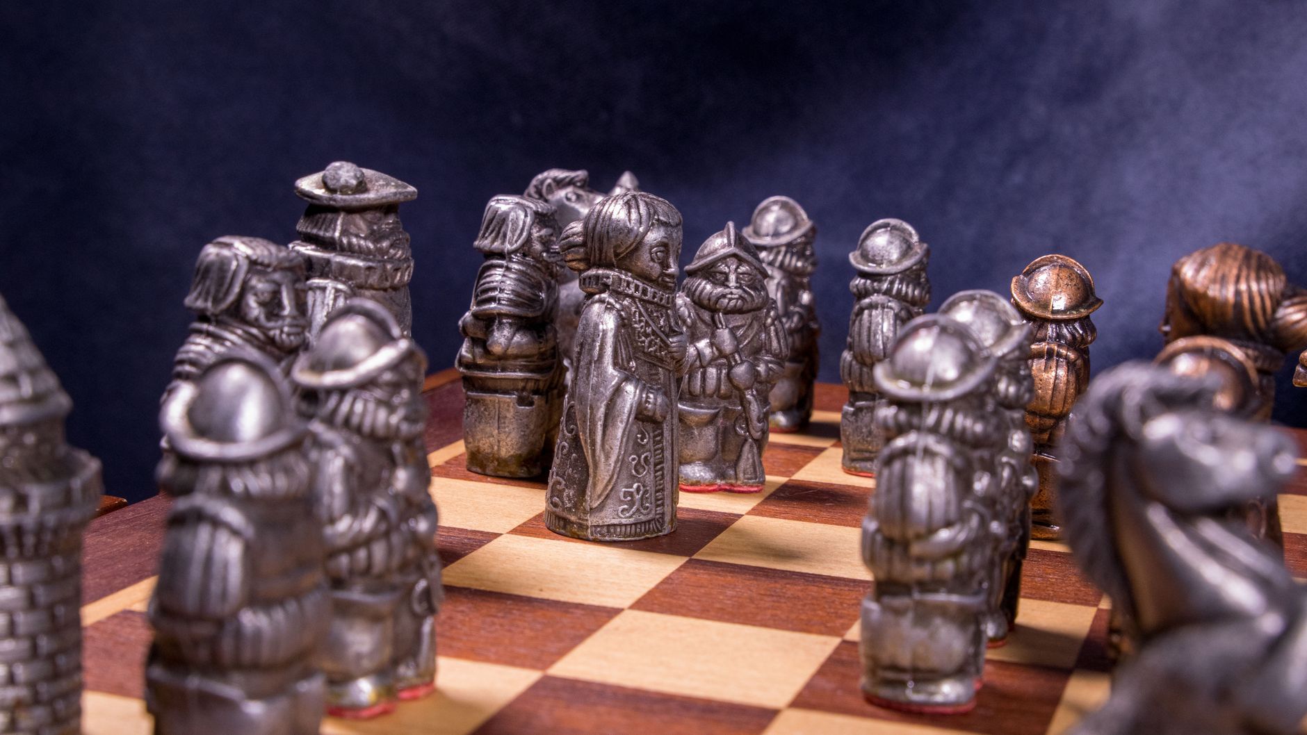 Intricate medieval-themed chess pieces set on a classic wooden board with a dramatic backdrop.