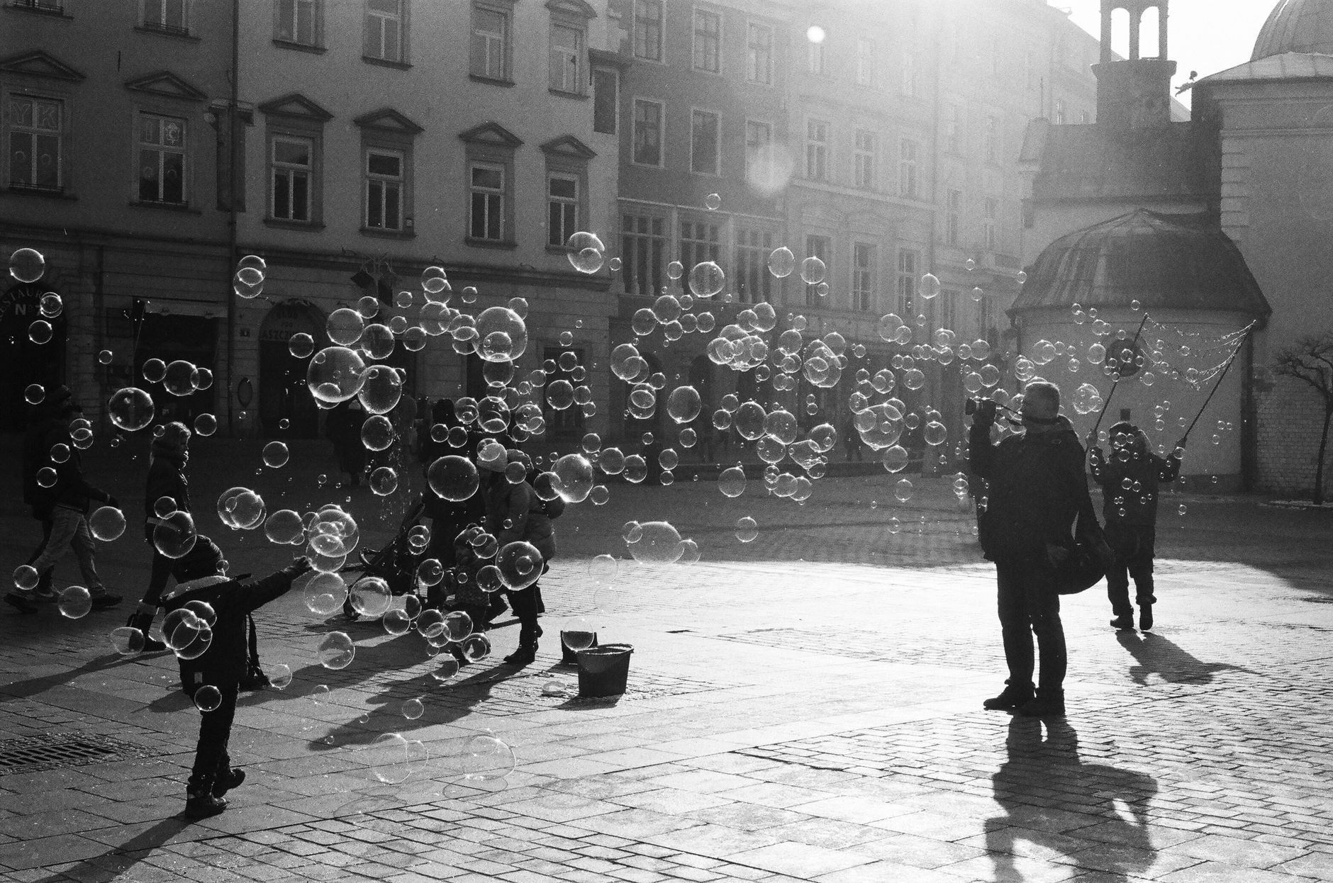A lively scene of children playing with bubbles in the town square of Krakow, Poland.