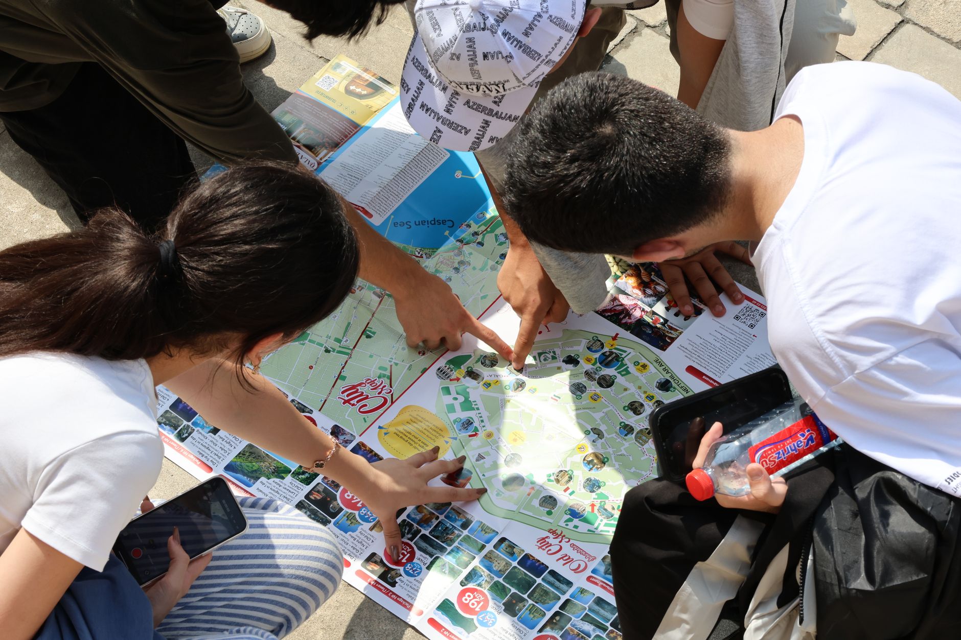 A group of young adults examining a city map outdoors, pointing excitedly at locations.