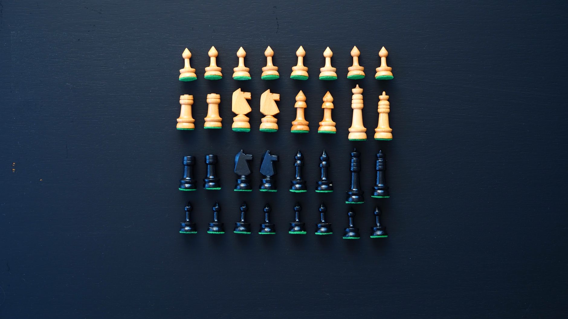 Top-down view of wooden and black chess pieces neatly arranged in rows on a black background.