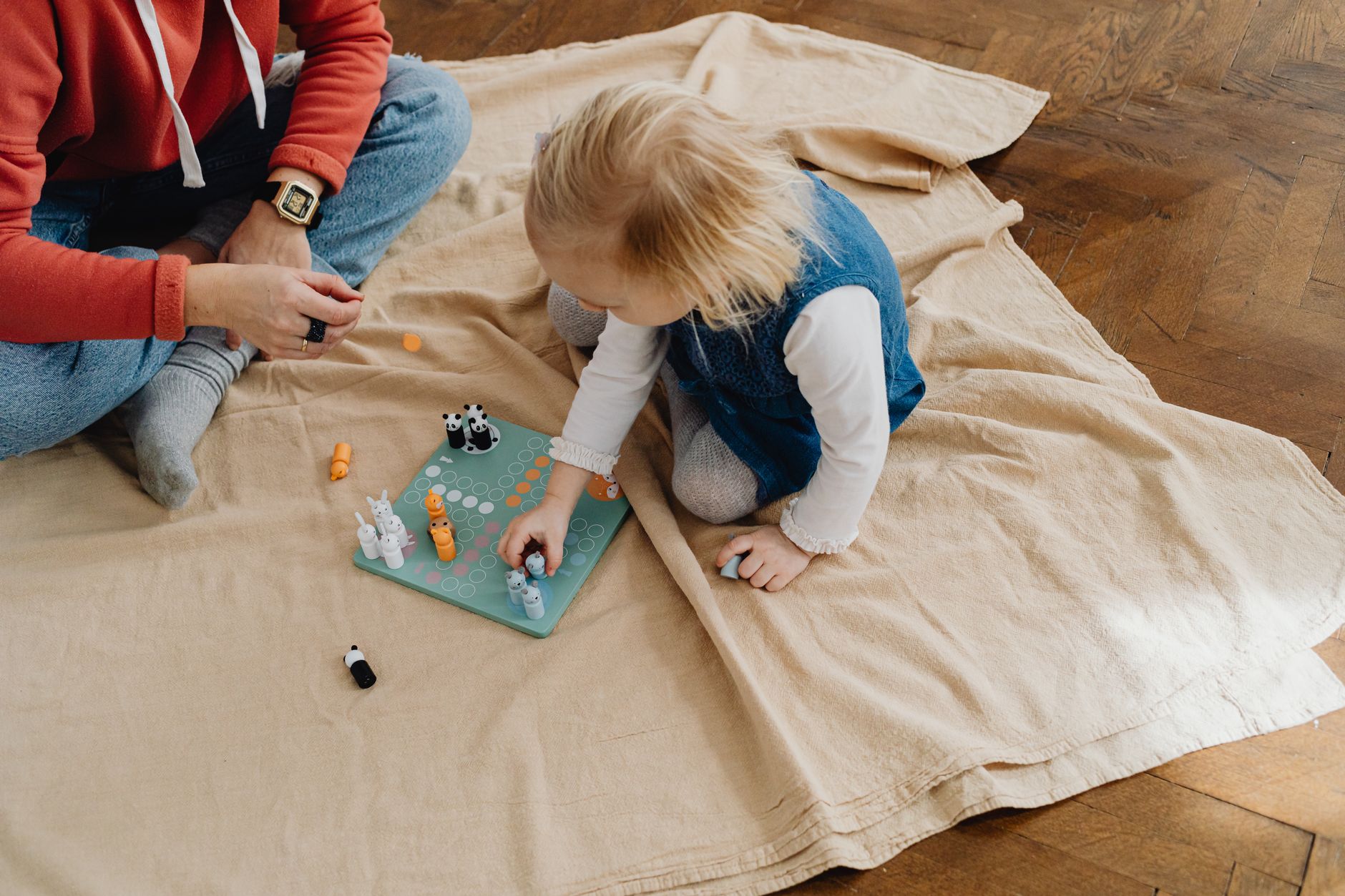 Child playing a board game with an adult on a wooden floor, enjoying indoor activities.