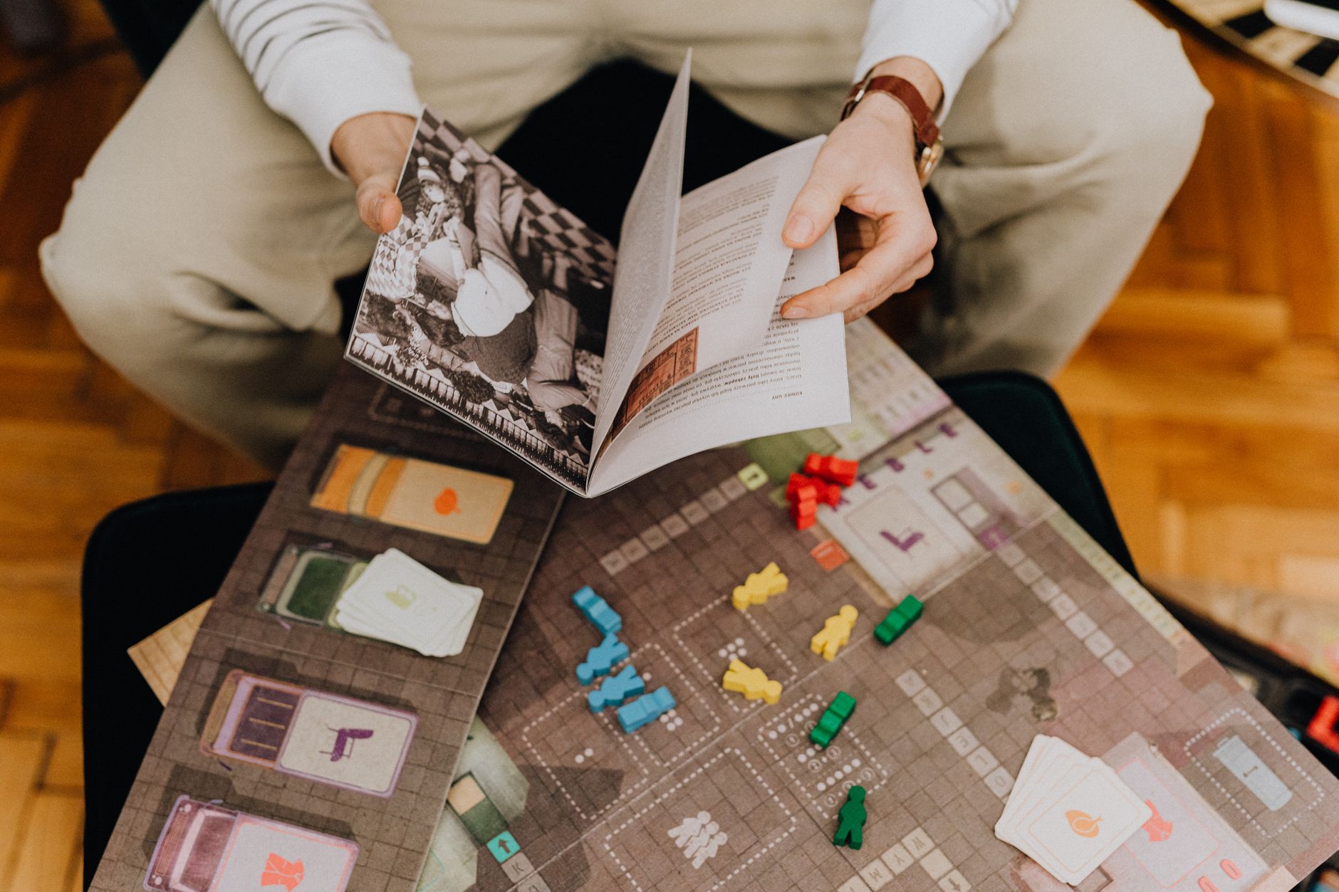 Detail of a person reading a board game manual with various game pieces.