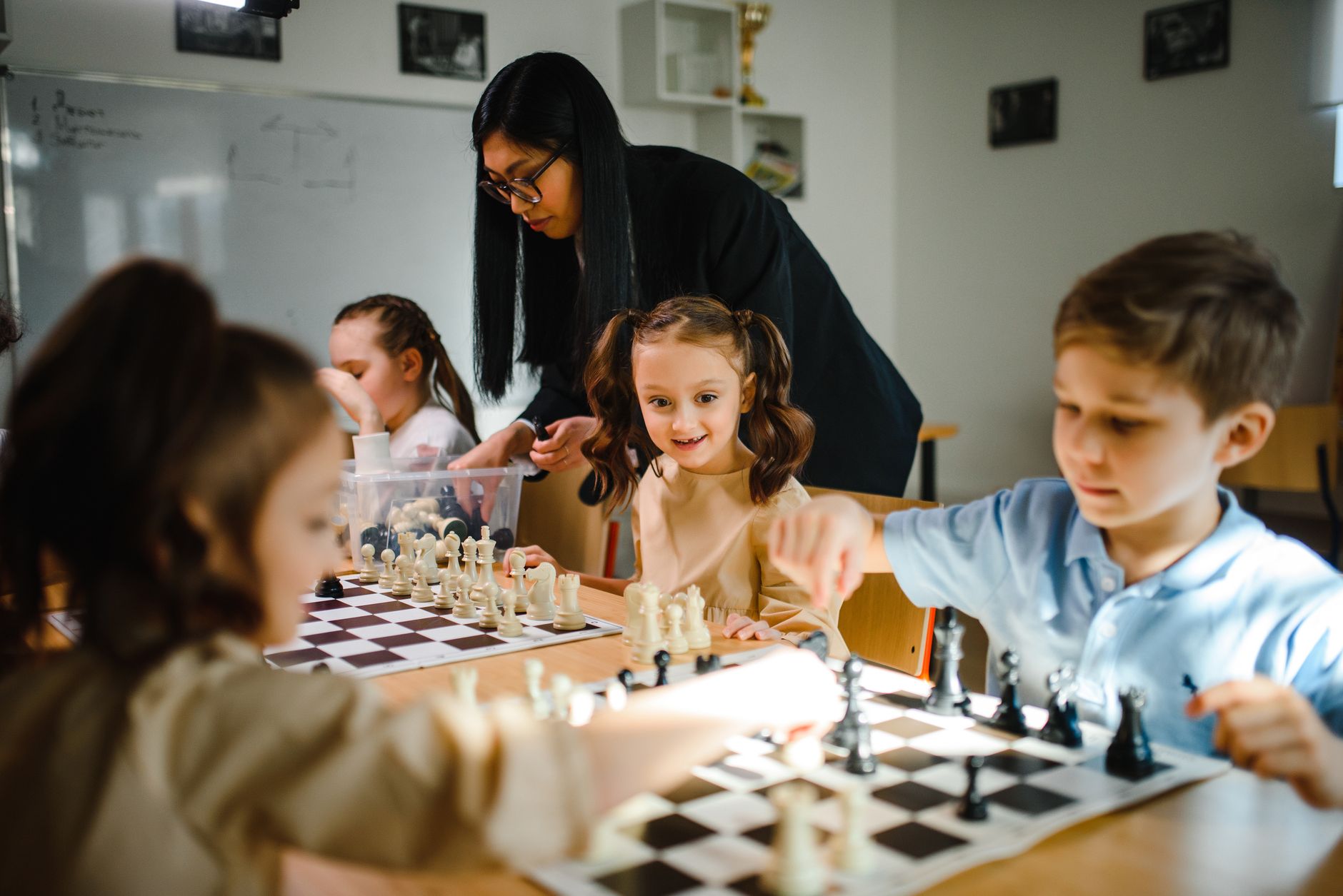 Kids engaging in a chess game with teacher guidance in a classroom.