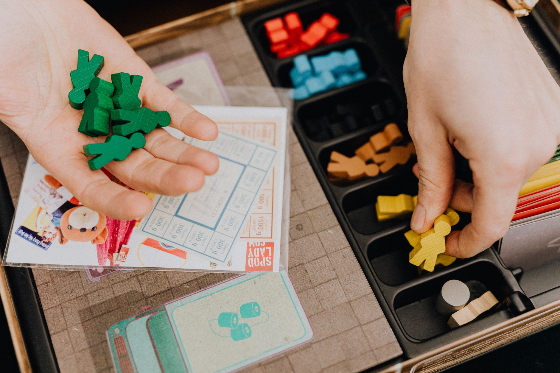 Hands organizing colorful game pieces on a board game set up for play session.