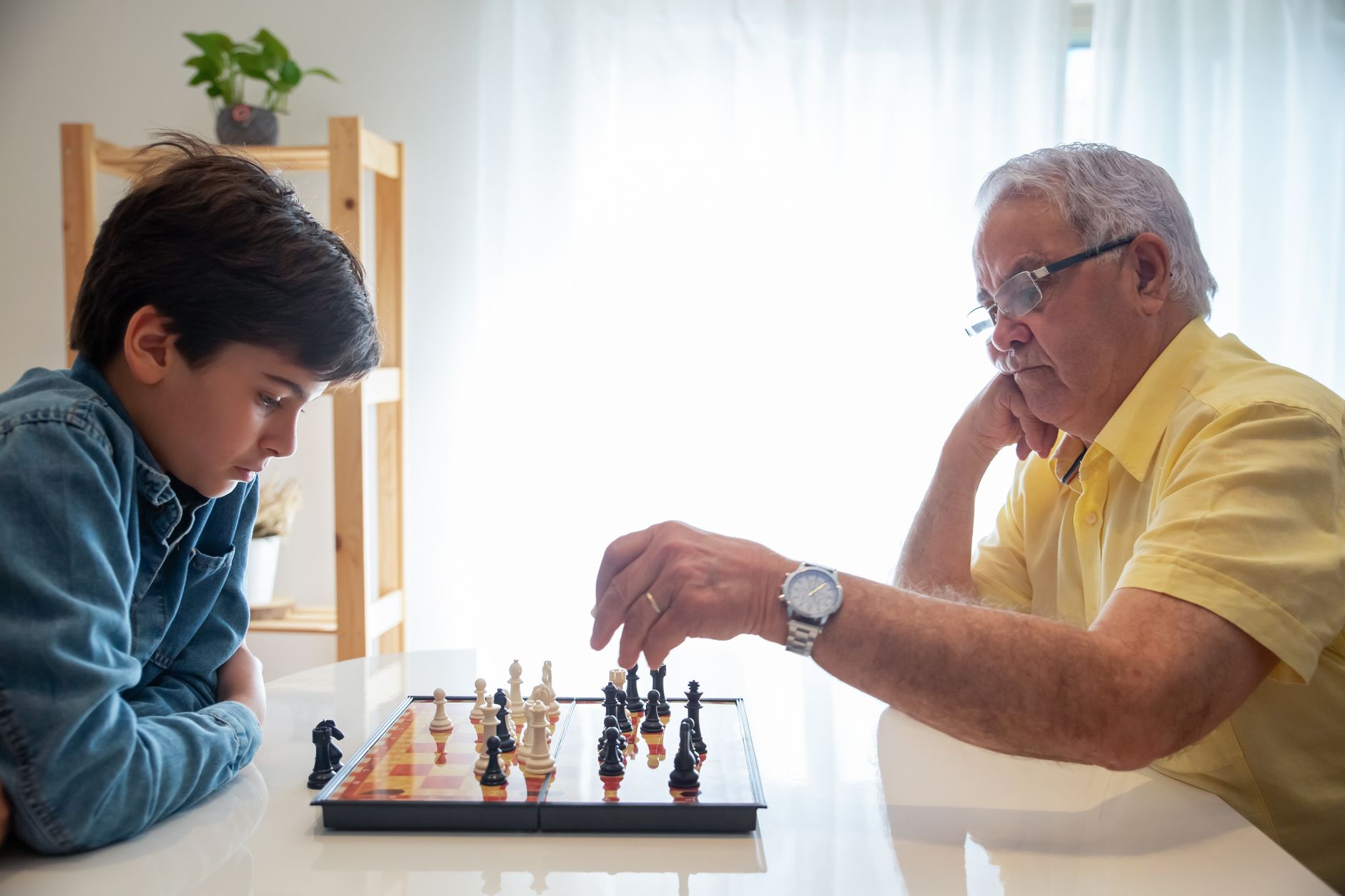 A thoughtful chess game between a grandfather and grandson indoors, promoting family bonding and strategy skills.