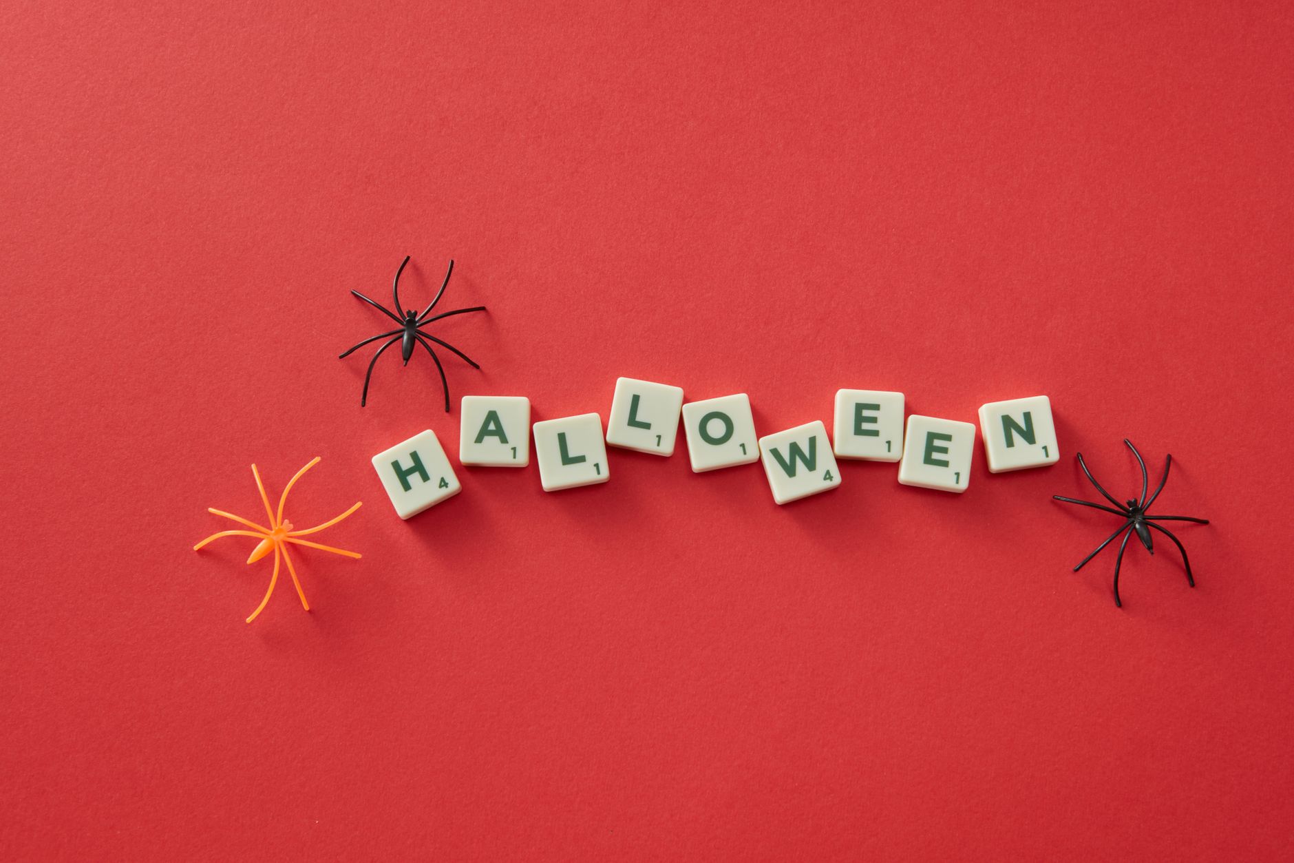 Scrabble tiles spelling 'Halloween' surrounded by spiders on a red background. Perfect for seasonal decoration.