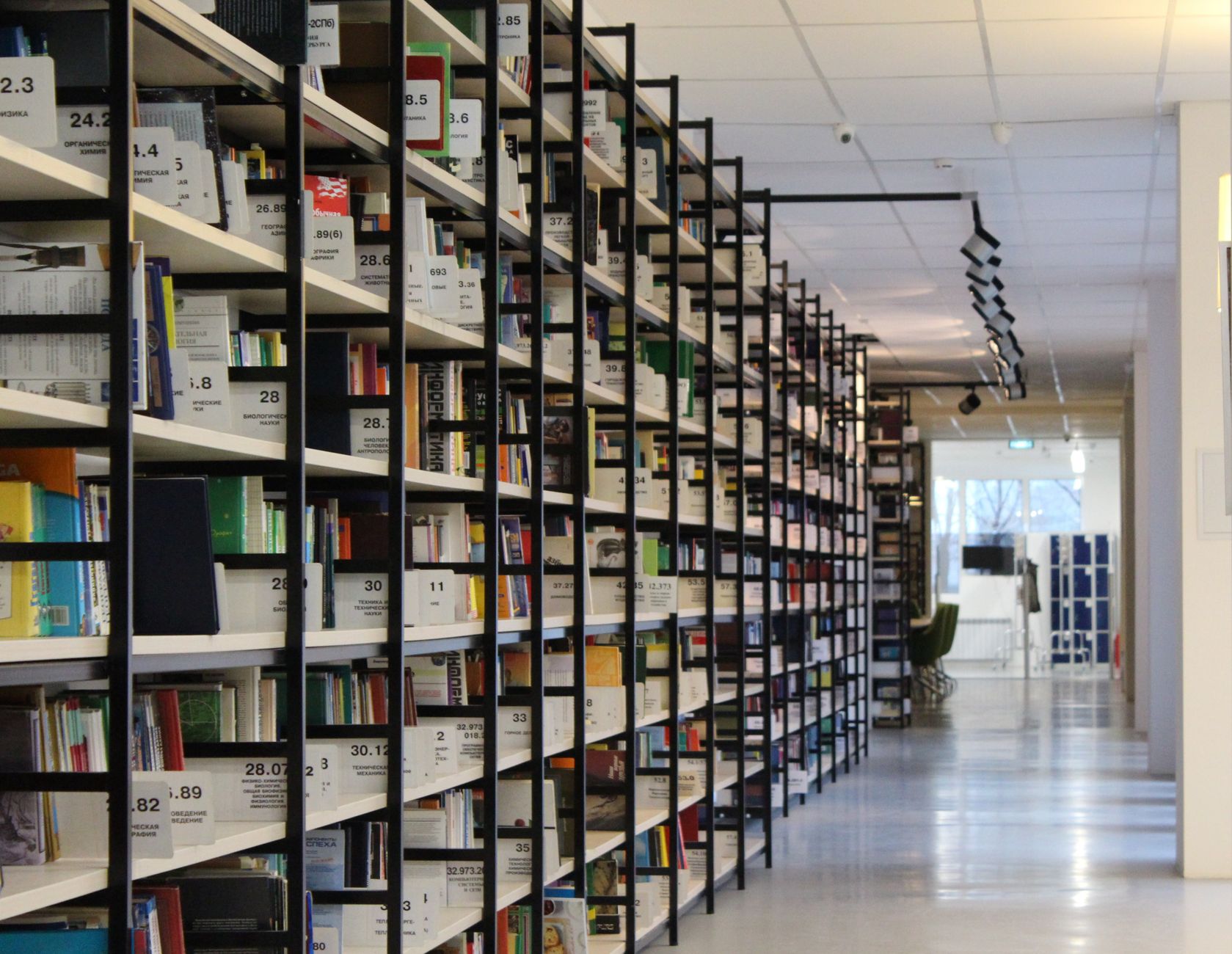 A spacious modern library with organized bookshelves and a well-lit aisle, perfect for reading and research.